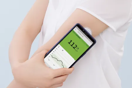 腕に貼ったセンサーにスマートフォンをかざして、グルコース値を読み取っているところ